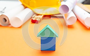 Small house model, hard hat and project blueprints on orange color background