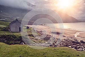 Small house by the ocean and beach, sun rise over a cliff and low cloudy sky. Keem beach, Ireland. Popular travel area, Irish