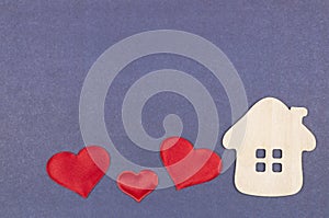 A small house and three red hearts on a gray-blue background. The concept of love, happiness in your home