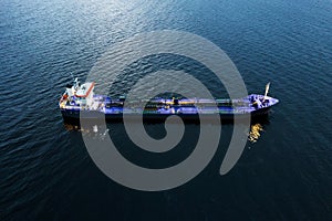 Small illuminated tanker ship with blue deck in the dark blue ocean water. Aerial view. Oil and gas transportation and supply.