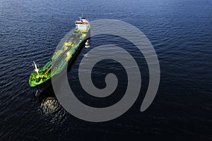 Small illuminated tanker ship with green deck in the dark blue ocean water. Aerial view. Oil and gas transportation and supply.