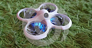 Small indoor home brushless fpv quadcopter lies on green carpet and flies away and shines with neon colorful lights