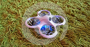 Small indoor home brushless quadcopter lies on carpet and is ready to fly and shines with neon colorful lights