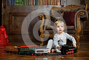 A small infant boy sits on the floor and plays a clockwork train