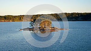 Small Island In Light Of Sunset In Sea Near The Shore With A Coniferous Forest