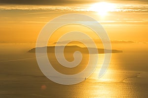 Small island and lonely sailing boat on the ocean during dramatic golden sunset near the coast of Trapani, on Sicily, Italy