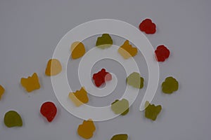 Small jelly candies in the form of yellow, red, green butterflies, shells, flowers located on a white plastic background.