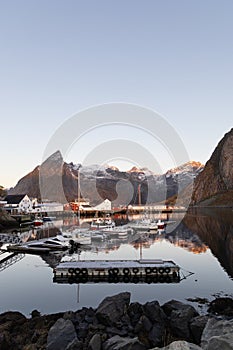 A small jetty with boats at Hamnøy with historic buildings and snowclad mountains in the background, Lofoten, Norway