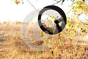 A small joyful boy in a yellow striped shirt swings in the middle of a rubber wheel of a swing