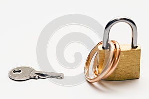 Small key and two golden wedding rings locked on a padlock