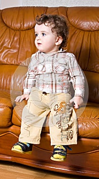 Small kid with curly hair on a leather brown sofa