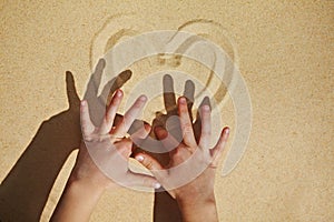 Small kid`s hands making a heart on beach sand