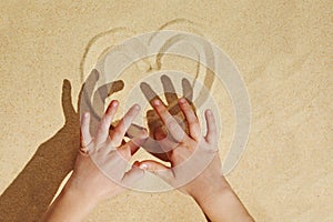 Small kid`s hands making a heart on beach sand