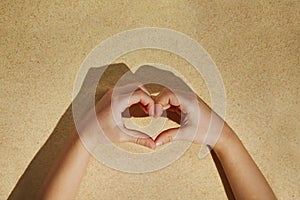 Small kid`s hands making a heart on beach sand