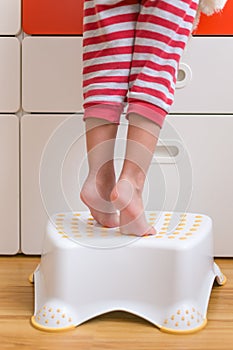 Small kids legs and feet tippy-toes on a step stool to reach for something on a cabinet counter