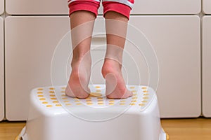 Small kids legs and feet tippy-toes on a step stool to reach for something on a cabinet counter