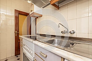 A small kitchen furnished with single wall cabinets, with antique ceramic hob, stainless steel sink with drainer and chrome faucet