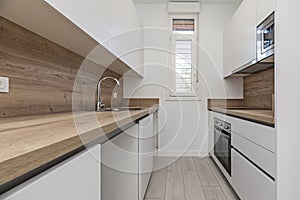 A small kitchen with smooth white furniture, wooden countertops that match the backsplashes, light parquet floors