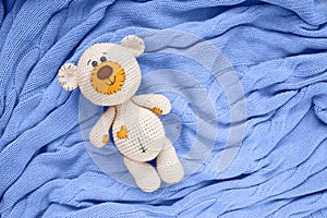 A small knitted amigurumi baby toy-bear is on a blue blanket, flat lay, top view