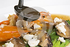 Small laddle is pouring sticky soy sauce to balnched kale and prawn shrimps and shitake and crab