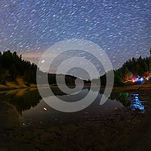Small lake under stars at night with short rails and camping at summer