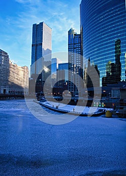 High-angle view of pedestrians on the riverwalk alongside a frozen Chicago River on a blue, frigid morning in winter.
