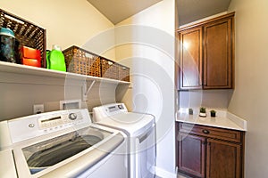 Small laundry room interior with washing mashines and dark wood storage cabinets