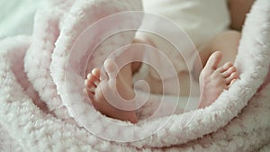 Small legs of a newborn close-up. The baby is lying in a cradle on a pink blanket