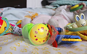 Small legs next to many toys on a light background. Legs in socks and pants. Rattles at the feet of the child. Close-up