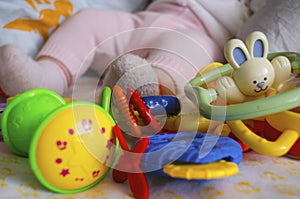Small legs next to many toys on a light background. Legs in socks and pants. Rattles at the feet of the child. Close-up