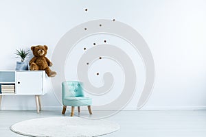 Small light blue armchair for kid standing in white room interior with stars on the wall, white rug and cupboard with