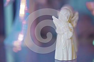 Small light white yellow marble figurine of an angel in dress on a pearlescent pink blue blurred bokeh