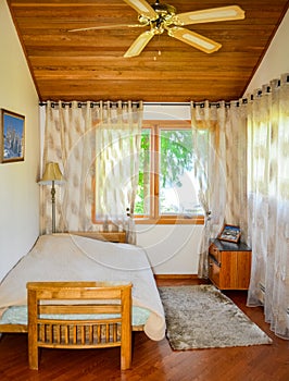 Small lightful bedroom with curtains on windows and rug on the floor.