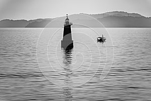 Small lighthouse and fishing boat on Japanese Seto Inland Sea with foggy mountains in background. Black and white photo