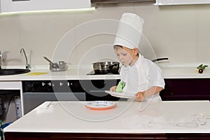 Small little boy in a chefs uniform wiping dishes