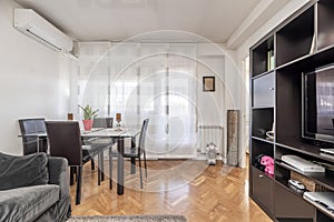 A small living room with a dark wood bookcase with a television inside and a dining table with a glass top