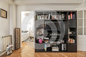 A small living room with a dark wooden bookcase with a television inside and access