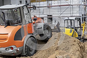 Small loader and excavator digger machine moving heap of earth and debris rubble at construction site. New building