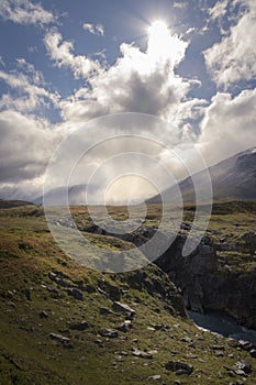 Small lonely hiker standing in enormous cloud and sunlight covered autumn wilderness