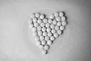 Small medical pharmaceptic round pills, vitamins, drugs, antibiotics in the form of a heart on a black and white background