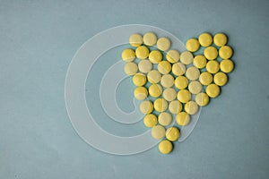 Small medical pharmaceptic round yellow pills, vitamins, drugs, antibiotics in the form of a heart on a blue background, texture.