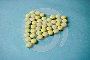 Small medical pharmaceptic round yellow pills, vitamins, drugs, antibiotics in the form of a heart on a blue background, texture.