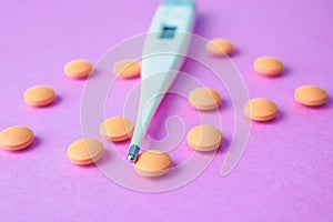 Small medical pharmacetic round pills, vitamins, drugs and electronic digital thermometer on a pink purple background.