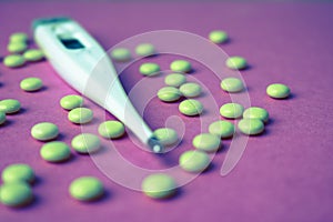 Small medical pharmacetic round pills, vitamins, drugs and electronic digital thermometer on a pink purple background.