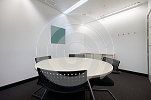 Small meeting room with white round circular table and whiteboard with soft markers and technical ceilings with track lamps