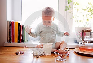 A small messy toddler boy sitting on kitchen counter at home, eating.