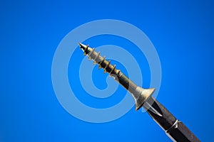 Small metal threaded screw held by screwdriver magnetic head. Close up studio macro shot, isolated on blue background