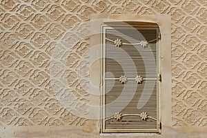 Small metallic door on the beige wall with sgraffito ornament in Segovia, Spain