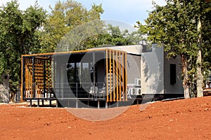 Small modern family holiday sea resort bungalow with large glass surface and front porch surrounded with tall trees in background