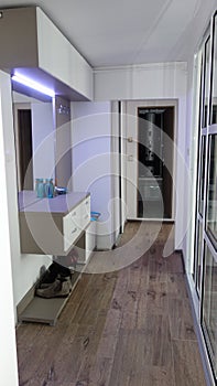 Small modernistic apartment hallway illuminated by led lights, big mirror, big glass door separating the kitchen